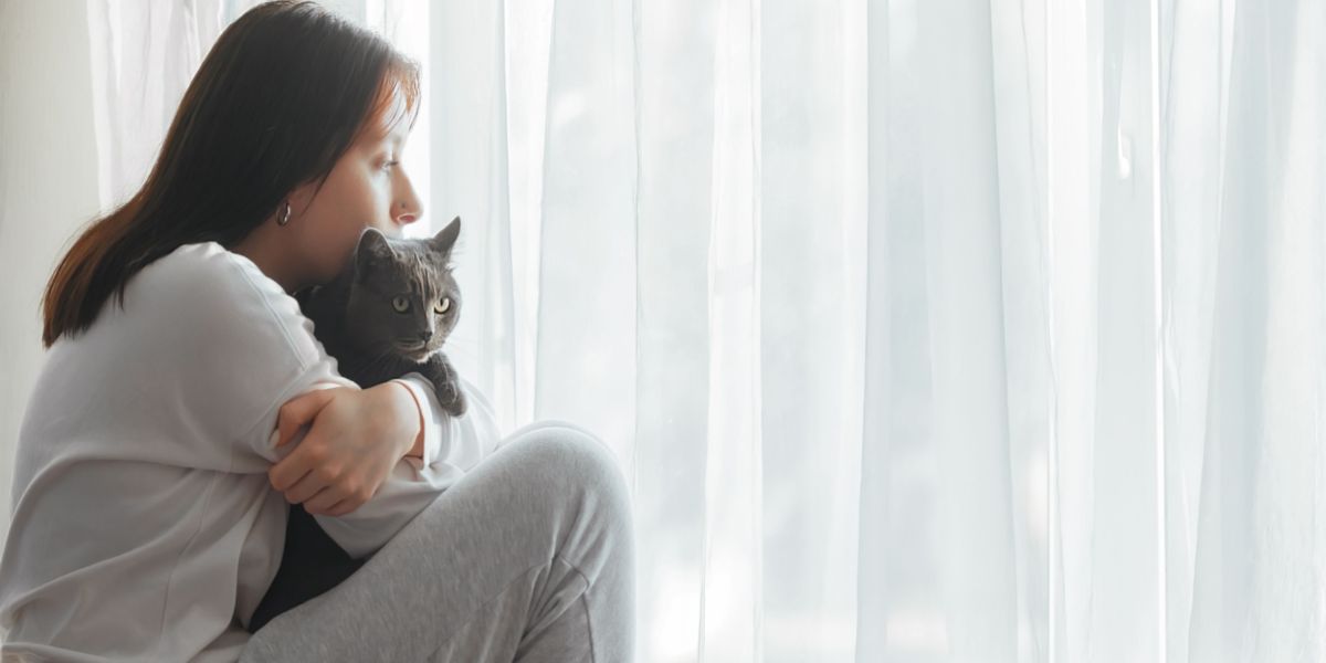 Imagem de uma mulher triste sentada com um gato, possivelmente indicando um momento de conforto ou apoio.