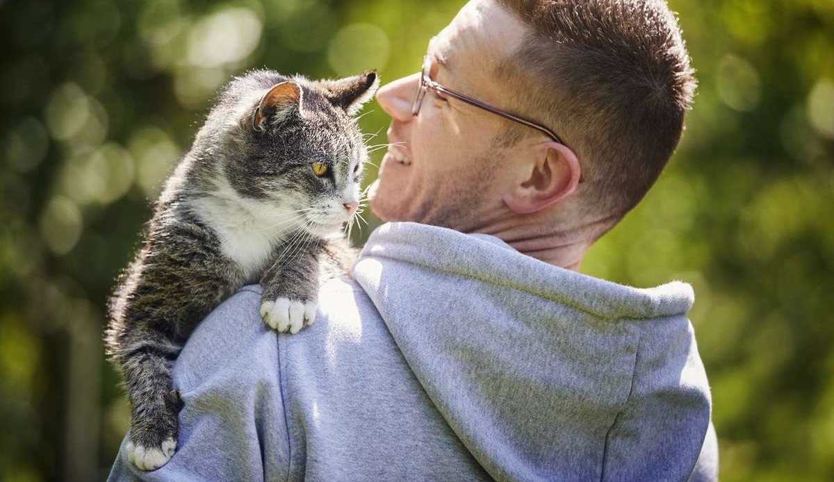 Homem sorridente carregando seu gato sênior no jardim